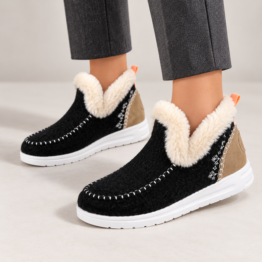 Black winter ankle boots worn by a model, showing plush collar, stitched toe and tan heel